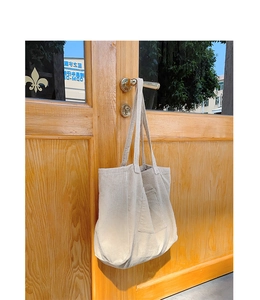 Close-up of beige corduroy tote bag with front pocket hanging on a wooden door handle