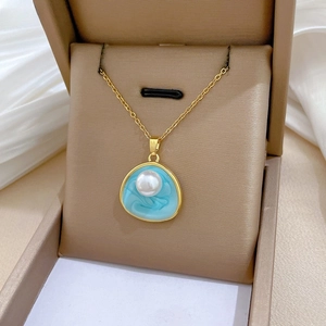Détail d'un collier doré avec perle et pendentif émail bleu sur boîte à bijoux beige