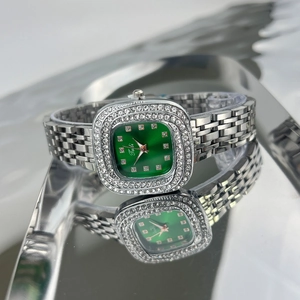 Macro shot of square green dial watch with diamond bezel on a reflective metal surface