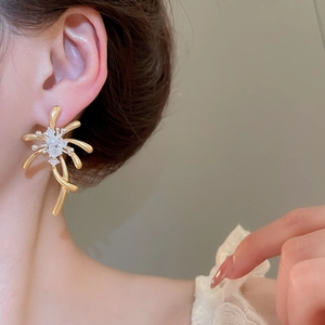 Detailed close-up of matte gold firework-shaped zircon earrings worn by a model