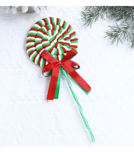 Detail of plush red and green spiral lollipop ornament with satin ribbon on white tablecloth