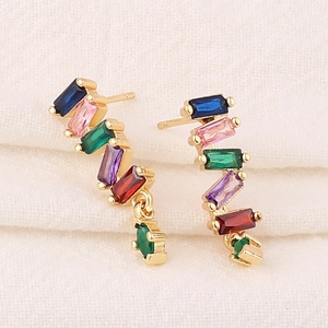 Elegant gold earrings with rainbow rectangular zircons on soft beige fabric background