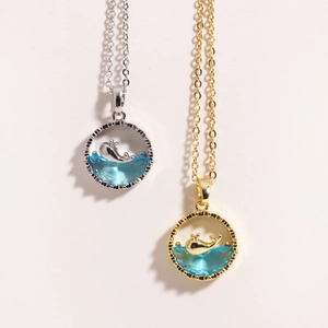 Detailed close-up of whale jumping over blue crystal pendant in gold and silver finish