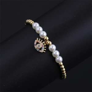 Macro detail of gold-plated evil eye charm and pearl beads on bohemian bracelet