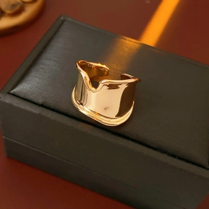 Detail of wide gold adjustable ring with irregular wavy edges on a black leather box