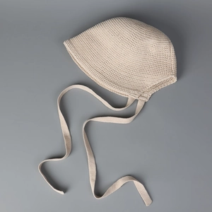 Close-up of beige knit bonnet featuring intricate hollow patterns and soft chin straps