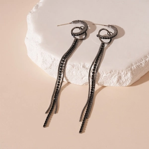 Macro detail of long black tassel earrings with dark crystal pavé on geometric metal rings