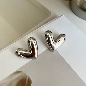 Macro shot of silver hollow heart stud earrings on white paper background