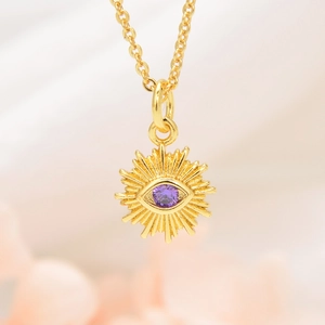 Detail of gold sunburst pendant necklace with a purple cubic zirconia eye inlay