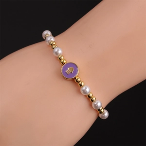 Detail of beaded Hamsa bracelet with white pearls and purple enamel charm on wrist