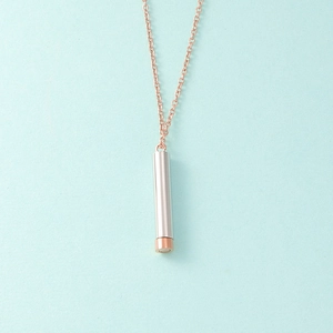 Detail of rose gold chain and silver cylindrical pendant on light blue background