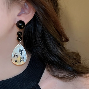 Detail of drop-shaped shell earring with floral print and black bead on model