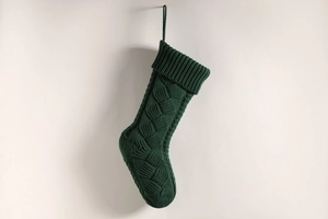 Detail of dark green cable knit Christmas stocking hanging on a neutral wall