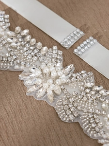 Macro detail of bridal belt with rhinestones, pearls and white satin ribbon on wood