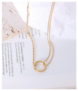 Close-up of asymmetric gold chain necklace featuring a polished ring pendant and double link