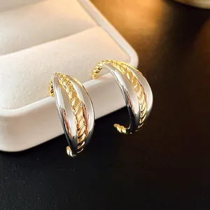 Detail view of irregular two-tone C-shaped hoop earrings with gold braided texture