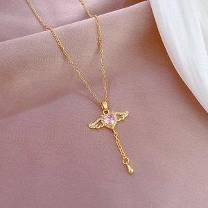 Close-up of heart wing pendant with pink stone and tassel on gold chain necklace