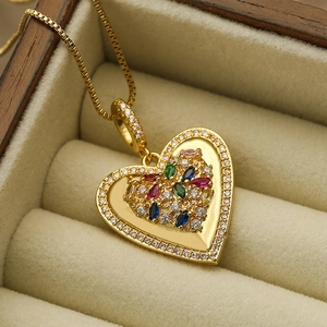 Elegant gold heart pendant necklace with colorful central gemstone in a beige jewelry box