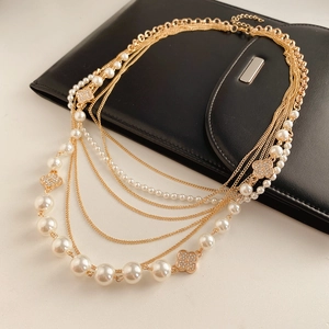 Detailed close-up of multi-layer gold chain necklace with pearls and crystal clover pendants