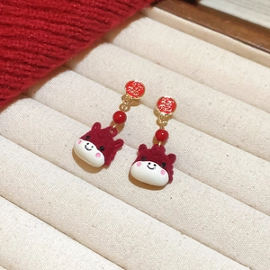 Close-up of festive red cartoon cow earrings with gold Fu character and velvet texture