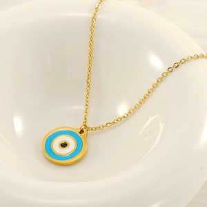Gold stainless steel evil eye pendant necklace with blue enamel on a ceramic tray