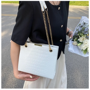Street style shot of white crocodile embossed tote bag with gold chain strap detail