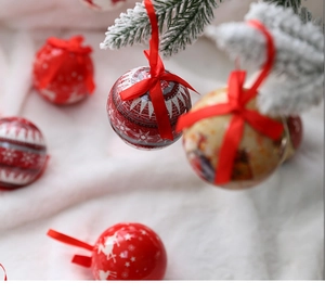 Close-up of a red Christmas ball with white reindeer patterns on snowy pine branches