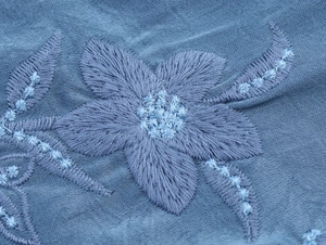 Vue détaillée de broderies florales complexes sur tissu bleu avec détails de couture