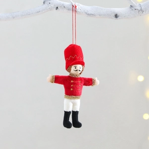 Plush Nutcracker soldier Christmas ornament hanging on a white branch with warm lighting
