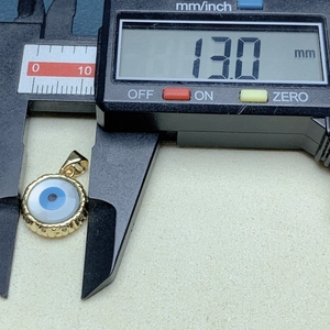 Digital caliper measuring the 13mm diameter of a gold Evil Eye shell pendant