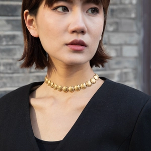 Detail of golden shell-link necklace worn by model against a rustic stone background