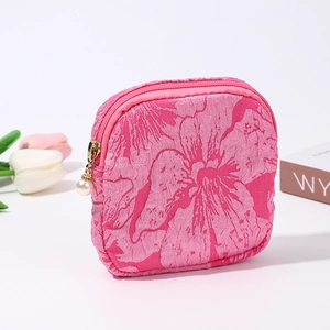 Pink jacquard mini cosmetic pouch with pearl charm detail on a clean white desk