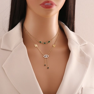 Close-up of gold double-layer necklace with emerald green gemstone and evil eye pendant