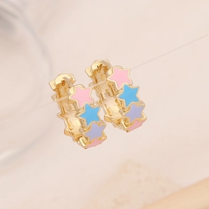 Macro shot of gold hoop earrings with colorful enamel star charms in pink, blue and purple