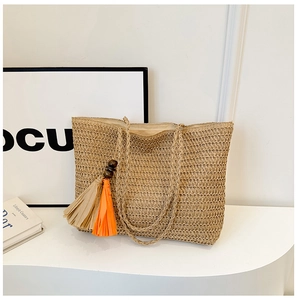 Close-up of khaki straw woven tote bag featuring orange beaded fringe tassel details