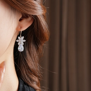 Close-up of silver flower and waterdrop zircon earrings on a model with soft focus