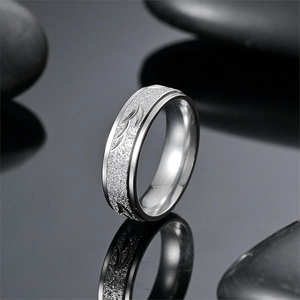 Detail of matte titanium steel ring featuring engraved leaf patterns on black pebble base