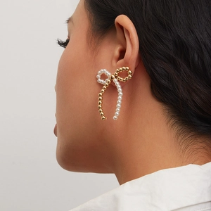Detailed view of a gold bow earring with faux pearls and long cascading tassels on a model