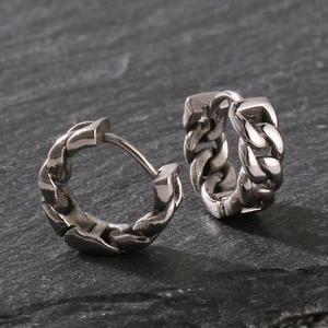 Detail view of vintage silver Cuban link earrings on a textured black stone surface
