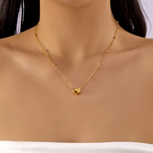 Detailed view of gold heart pendant necklace with beaded chain on a model's neck