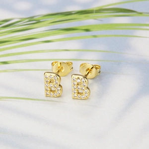 Macro detail of gold-plated B-shaped stud earrings with micro-pave white zircon crystals