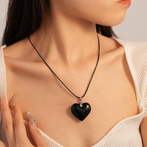 Close-up of a vintage black heart pendant necklace on a leather cord worn by a model