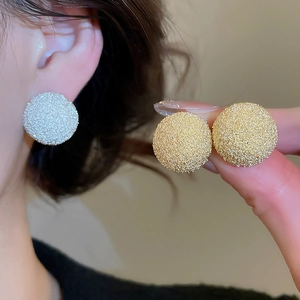 Close-up of textured gold and silver round stud earrings with frosted metallic finish