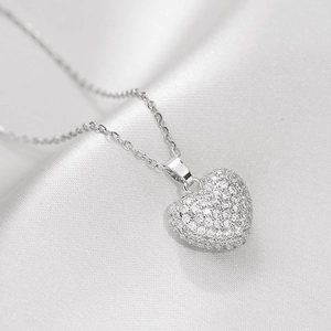 Macro shot of a sparkling crystal heart pendant with silver link chain on white silk