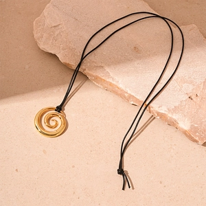 Close-up of golden spiral pendant with black cord on a natural textured stone background