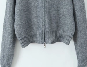 Detail view of the ribbed knit hem and metallic zipper on this grey cardigan sweater