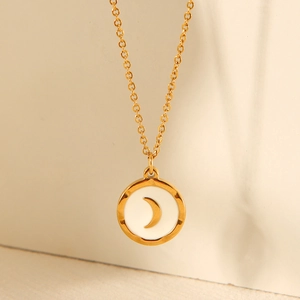 Detail of a gold necklace featuring a round pendant with a white inlay and crescent moon