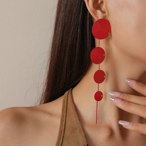 Detail of red long fringe earrings with four tiered textured circular discs on a model