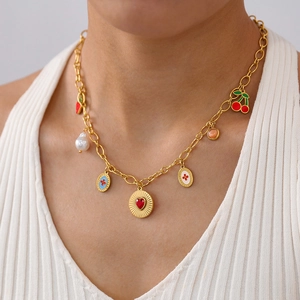Close-up of gold necklace featuring cherry, pearl, and heart pendants on a model