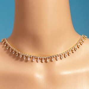 Detail of gold plated tennis necklace with teardrop zircon charms on a beige bust